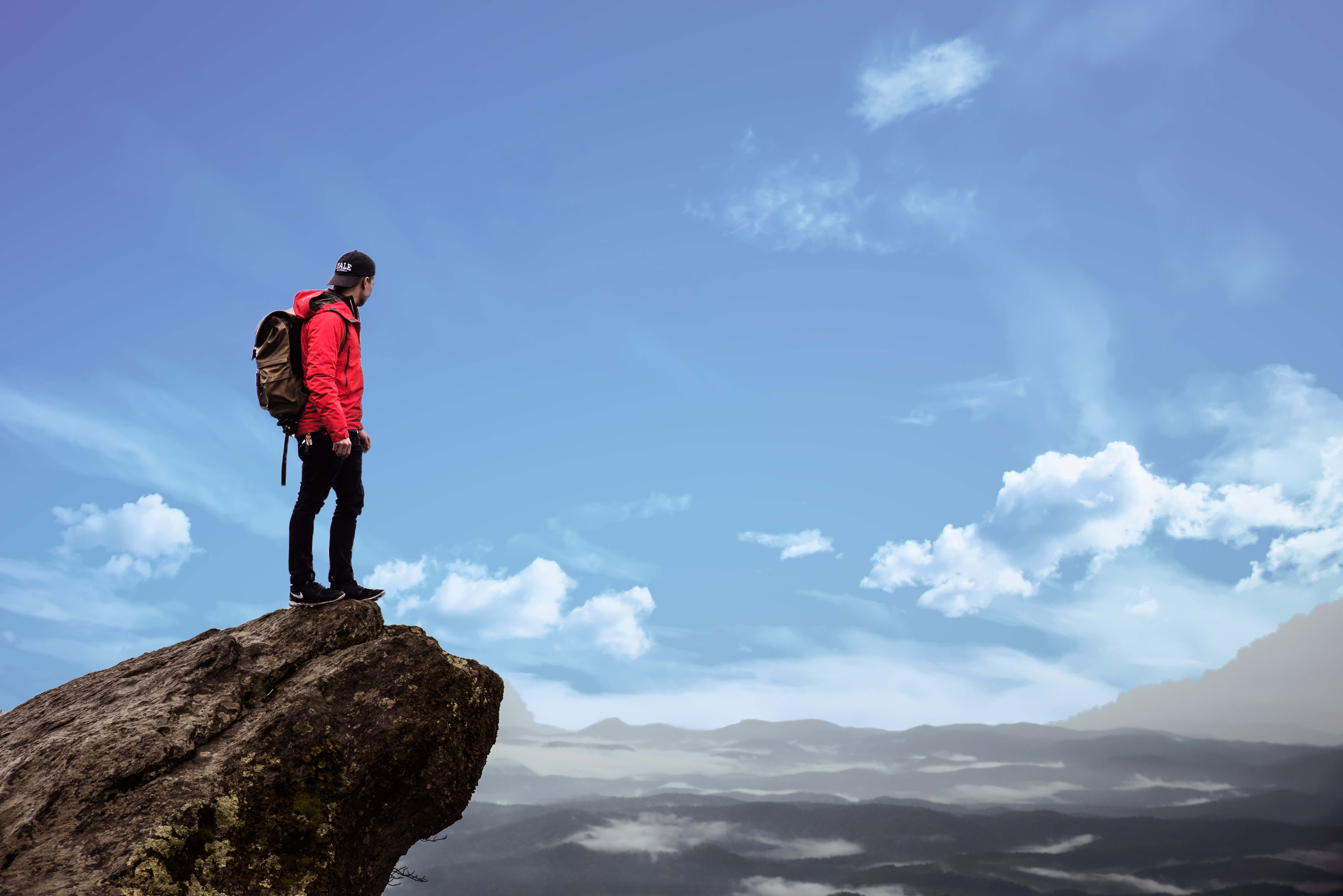 Man in orange jacket standing on a cliff, looking out at the view