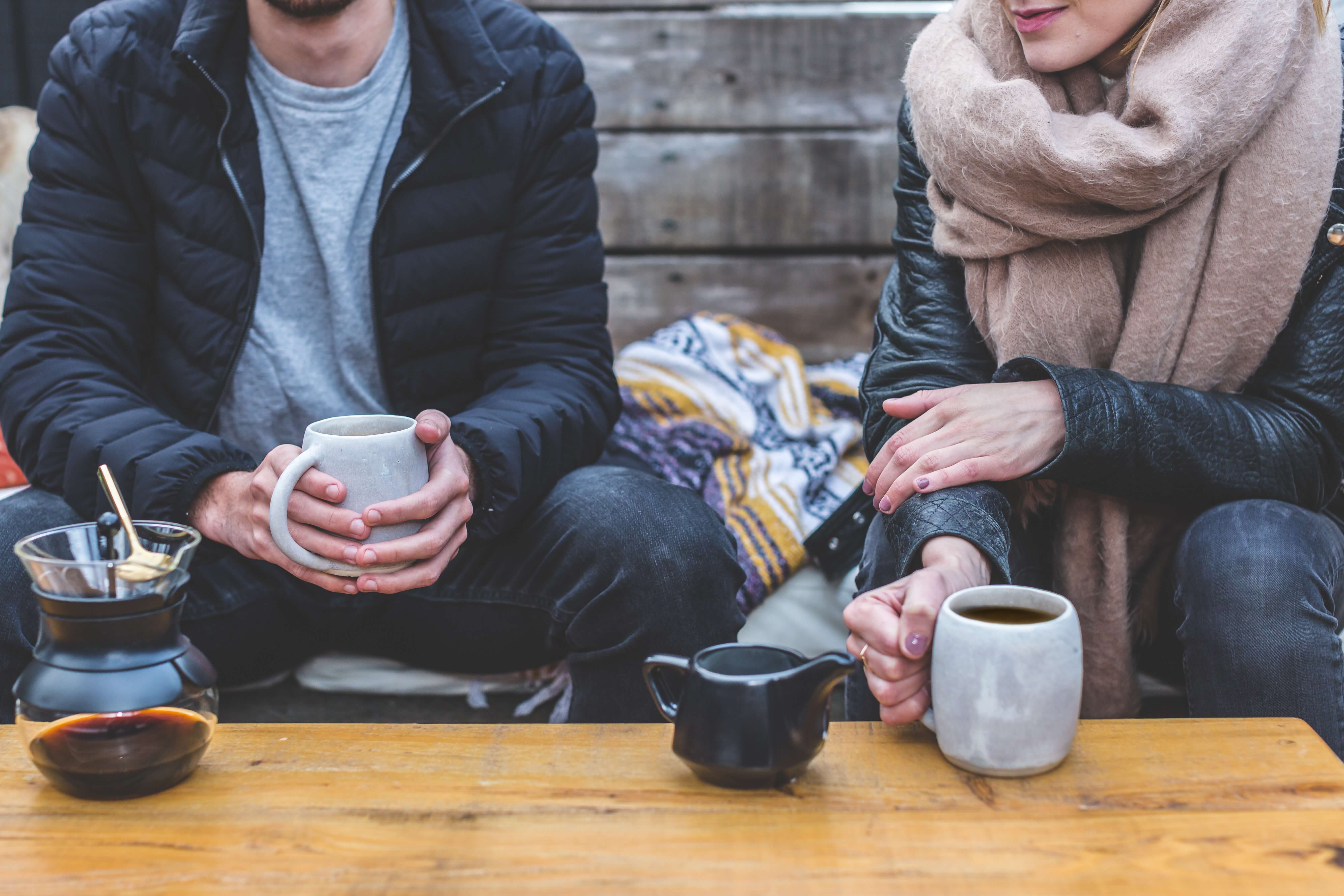 Man and woman sitting at a table holding mugs filled with coffee